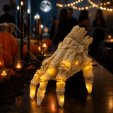 Skeleton hand lit on a party table with candles and guests in the background